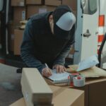 Home Courier organizing packages from a van, preparing for delivery in a logistics setting.